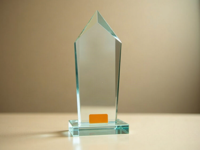A clear glass award trophy on a beige counter with a small orange sticker over its base plate